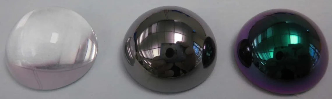 Three 16 mm glass half-spheres side by side: one uncoated, one coated with titanium carbide, and one with a further oxide layer whose green and purple interference color is even across the whole curved surface